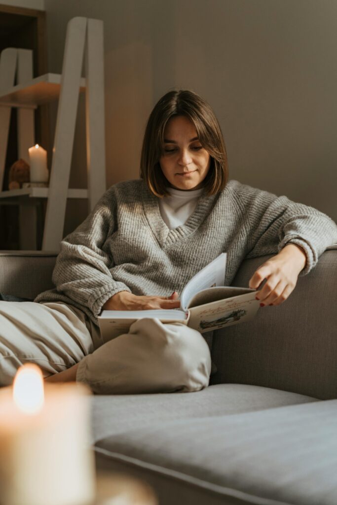 Woman in a cozy sweater reading a book on a comfortable sofa, creating a warm, serene atmosphere.